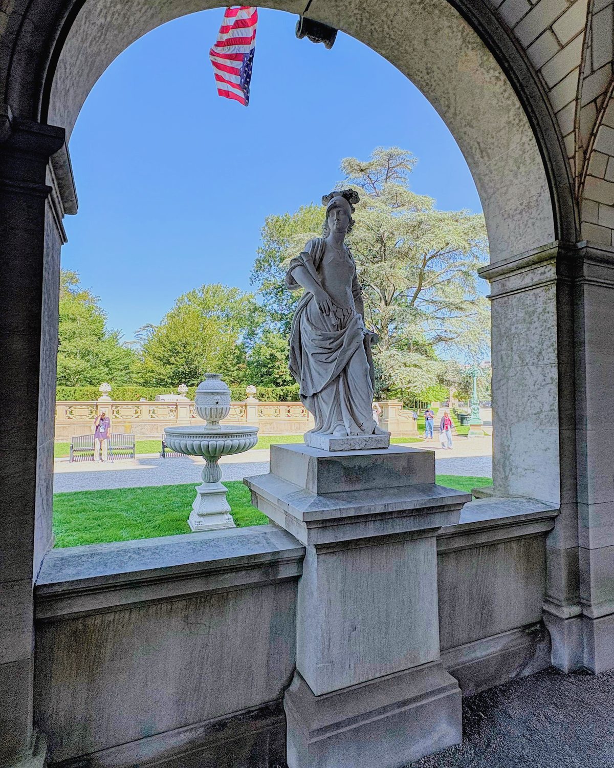 A stone arch framing a statue and fountain on the lawn beyond